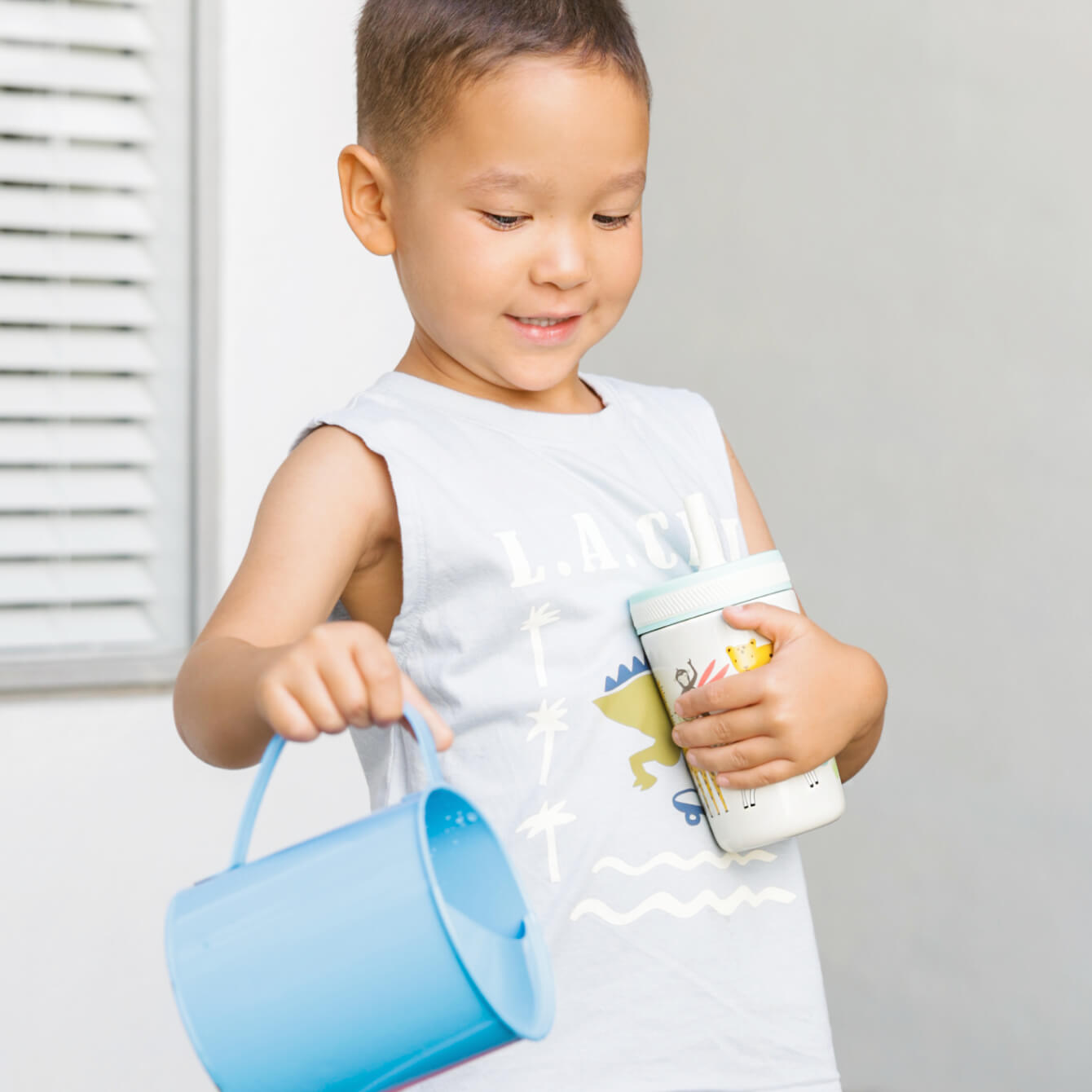 boy pouring water from a jug while holding a straw cup