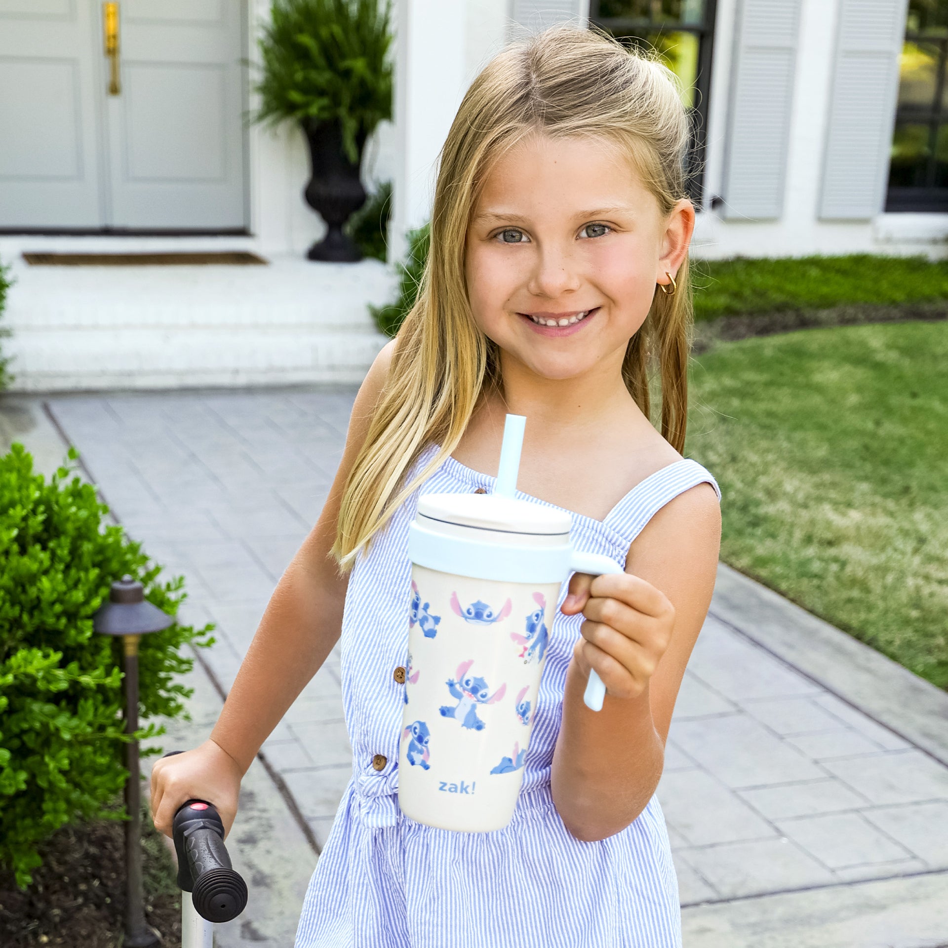 Young girl holding a Lilo & Stitch tumbler with a straw, standing outside a house.