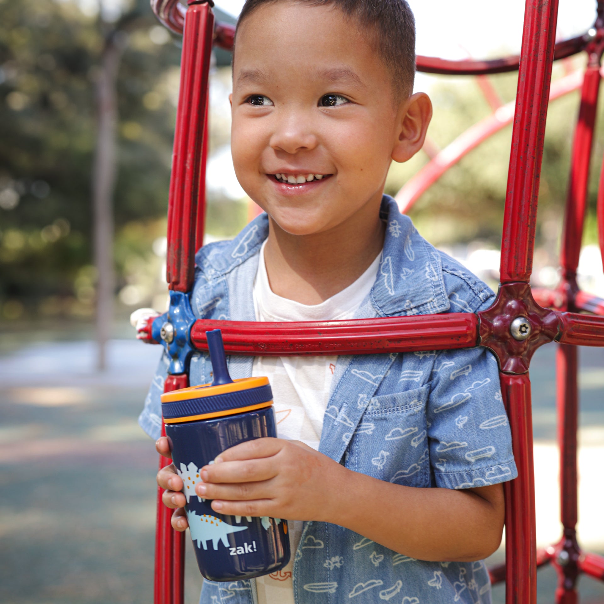 Boy holding zak! dinosaur leak-proof kids cup at the playground